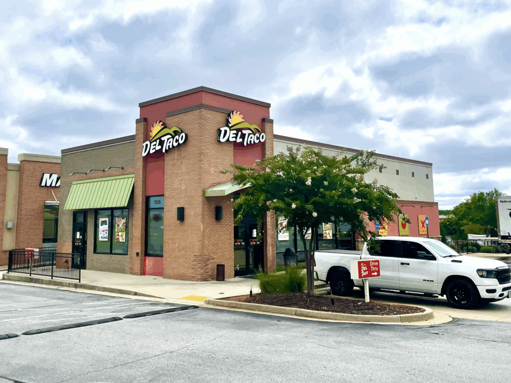 A Del Taco fast food restaurant in Metro Atlanta with a white pickup truck parked outside under a cloudy sky, showcasing the popularity of drive thru restaurants.