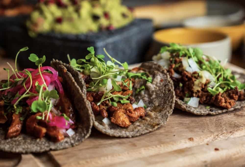 Three mexican tacos on a wooden cutting board.
