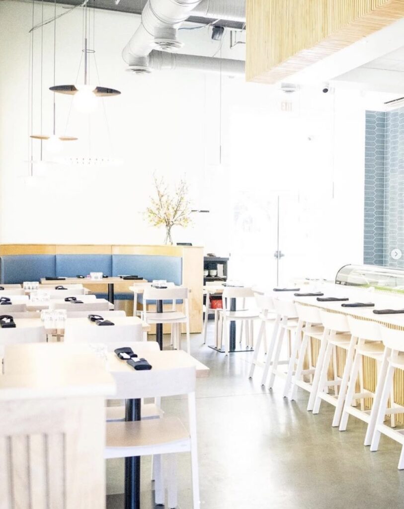 Bright, modern restaurant interior with wooden tables and chairs, minimal decor, and large windows.