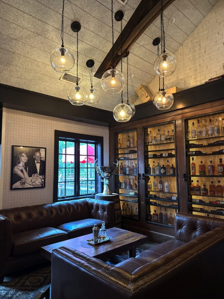 A room with bookshelves filled with bottles, leather sofas, hanging glass globe lights, and a framed picture on the wall.