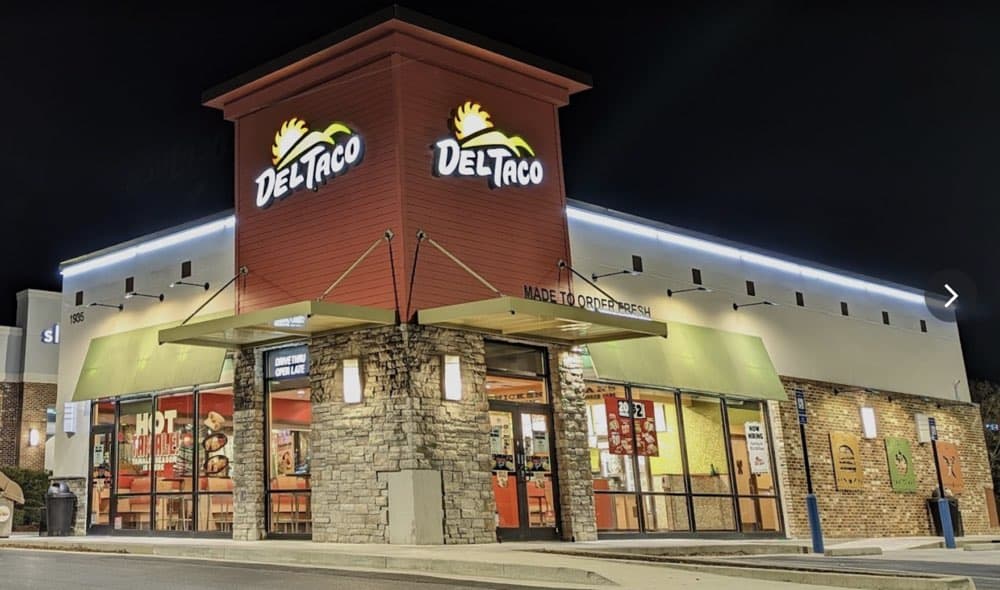A brightly lit Del Taco restaurant at night, featuring illuminated signage, large windows, and stone accents on the exterior.