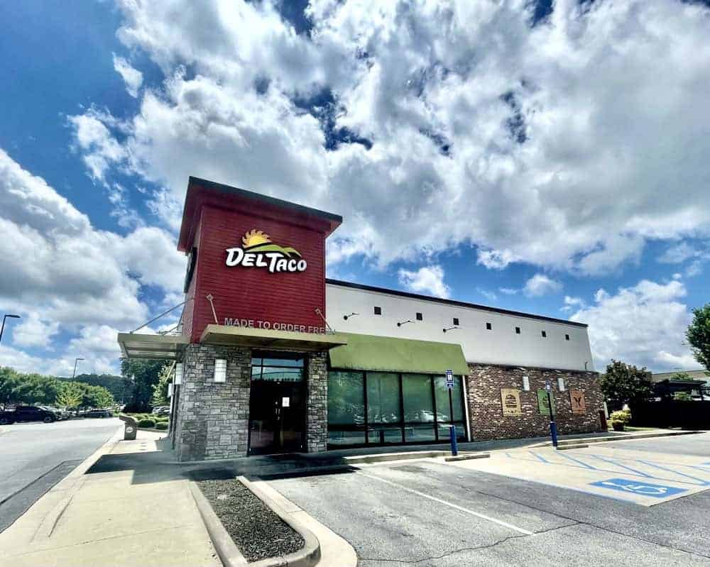 Exterior of a Del Taco restaurant in Metro Atlanta on a sunny day, featuring an empty parking lot with marked accessible spaces and drive thru service, perfect for those seeking drive thru restaurants or a potential Del Taco lease.