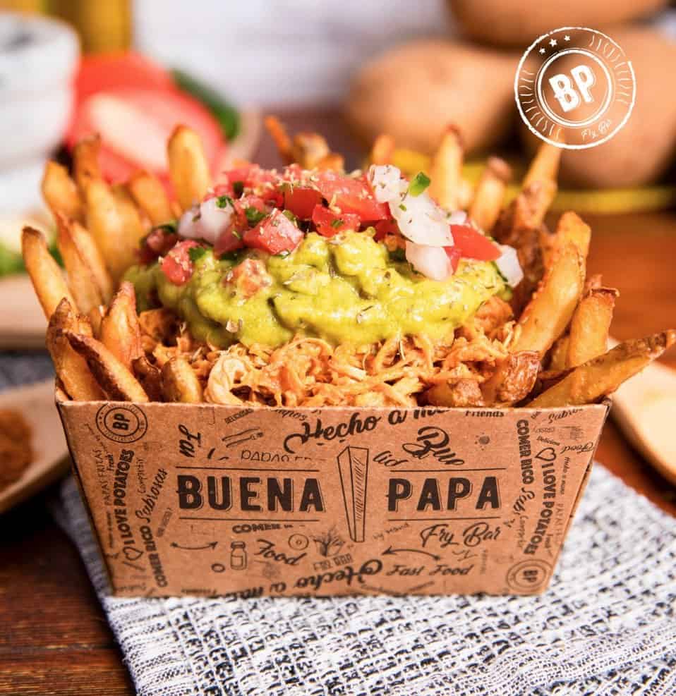 A serving of loaded fries topped with shredded meat, guacamole, and diced tomatoes, presented in a branded paper container at TKO @ Southern Feed Store.