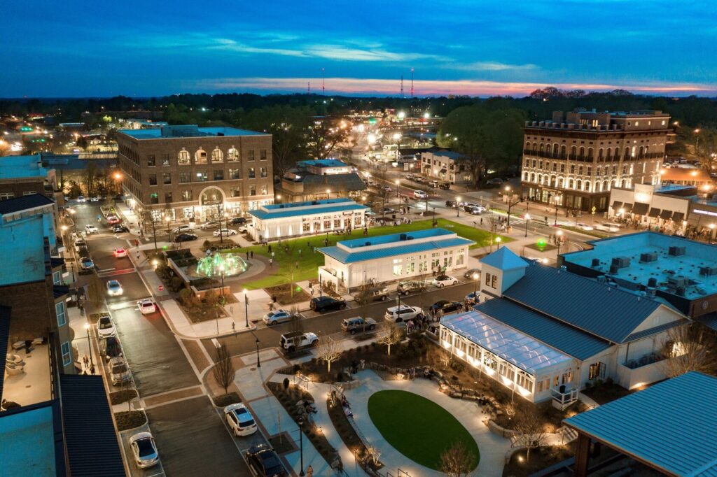 Aerial view of a town center at dusk with illuminated buildings and streets, featuring "Where's The Scoop?" cafe for sale in Alpharetta, GA.