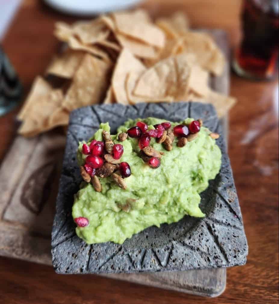 A plate of guacamole with pomegranate and chips.