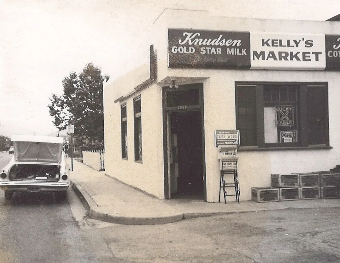 A small corner store called Kelly's Market with signs including Knudsen Gold Star Milk. There is a vintage car parked at the curb, and a mailbox and some crates are outside the store.