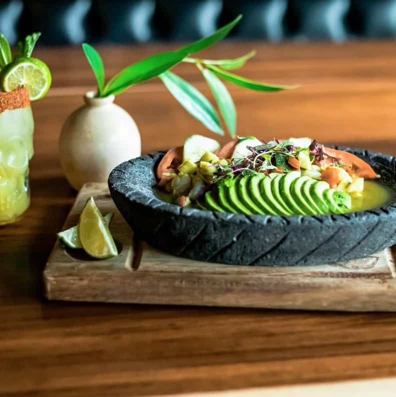 A bowl of guacamole and lime on a wooden board.