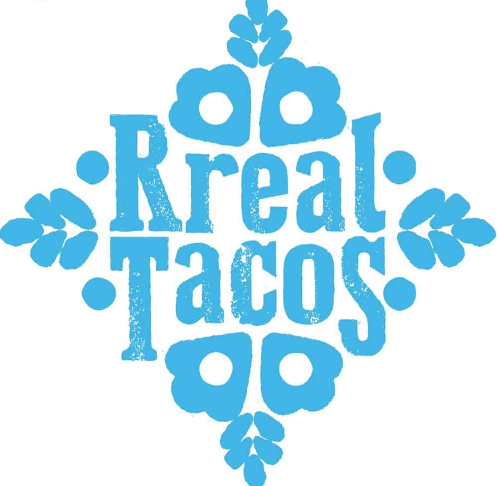 Blue decorative logo with the words "Real Tacos" in bold, distressed font, surrounded by symmetrical floral and heart motifs on a white background.