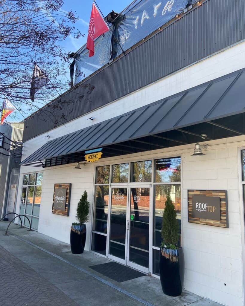 Modern restaurant storefront with glass doors, potted plants, and signage.