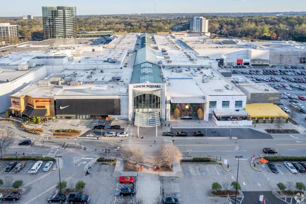 Aerial view of a large shopping mall with a prominent entrance labeled "Lenox Square." Several cars are parked in the lot, with stores and trees visible in the background.