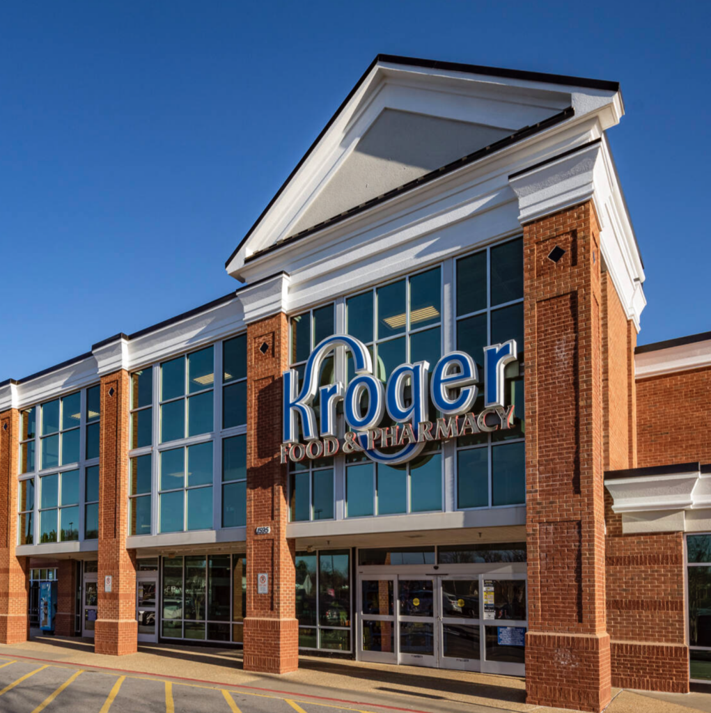 The exterior of a Kroger Food & Pharmacy store, with its large windows and brown brick facade, stands proudly under the clear blue sky, reminiscent of a bustling sushi restaurant in downtown Cumming, GA.